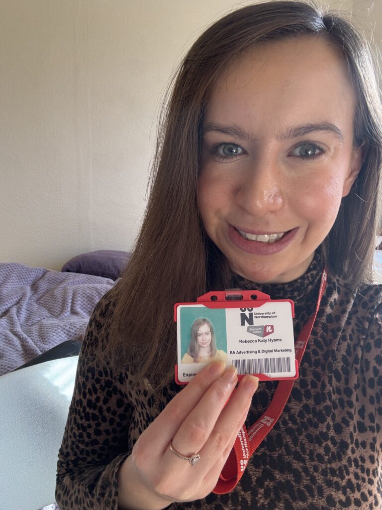 Selfie of Becky, white female with brown hair, smiling and holding up her University student ID and lanyard